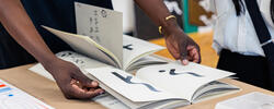 A person wearing a gold bracelet is opening a book that is part of a display table.