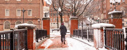 A person wearing a winter coat and boots walks across the College Street bridge in the snow.