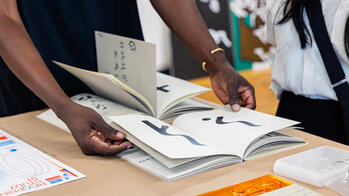 A person wearing a gold bracelet is opening a book that is part of a display table.