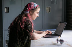 A student with a multicolored scarf on their head is looking at computer.